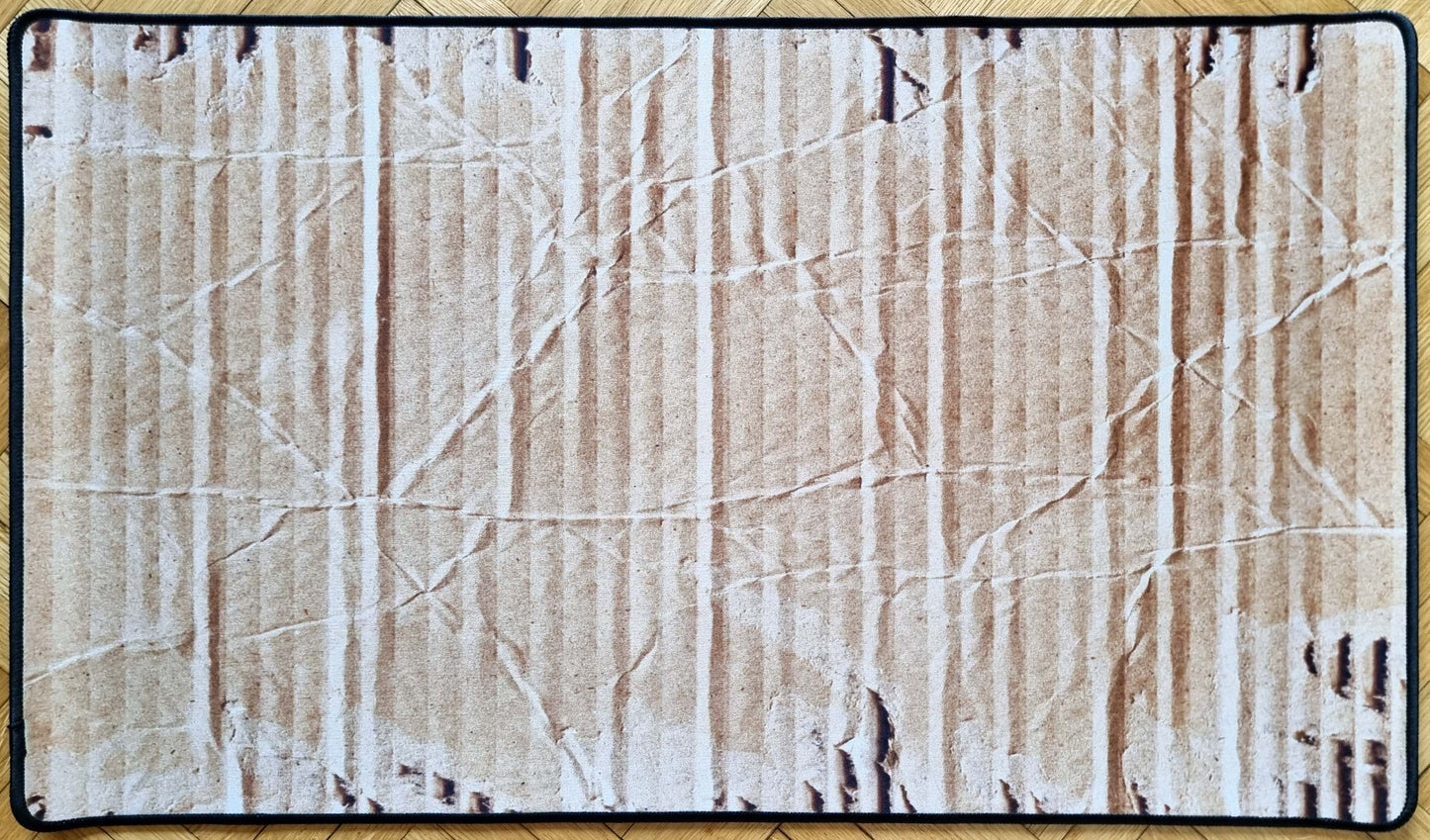 Stitched cardboard texture TCG playmat showing a realistic worn corrugated box surface with creases, vertical ribs, scuffs, and a black border.