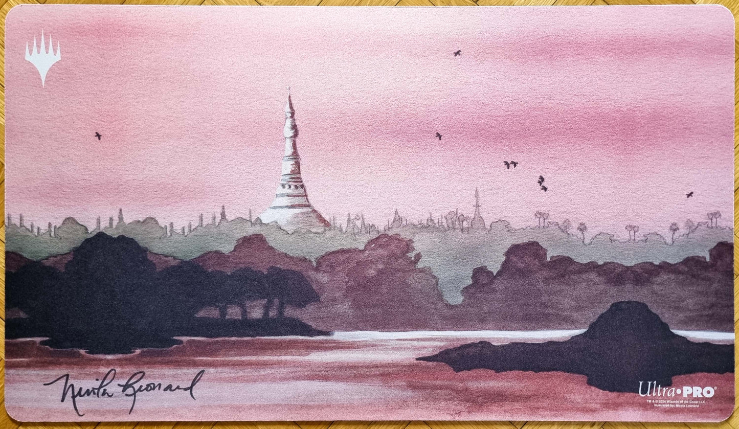 Signed Karakas MTG playmat by Nicola Leonard with the newer Magic logo, showing a pink landscape, distant tower, water, and silhouetted scenery.
