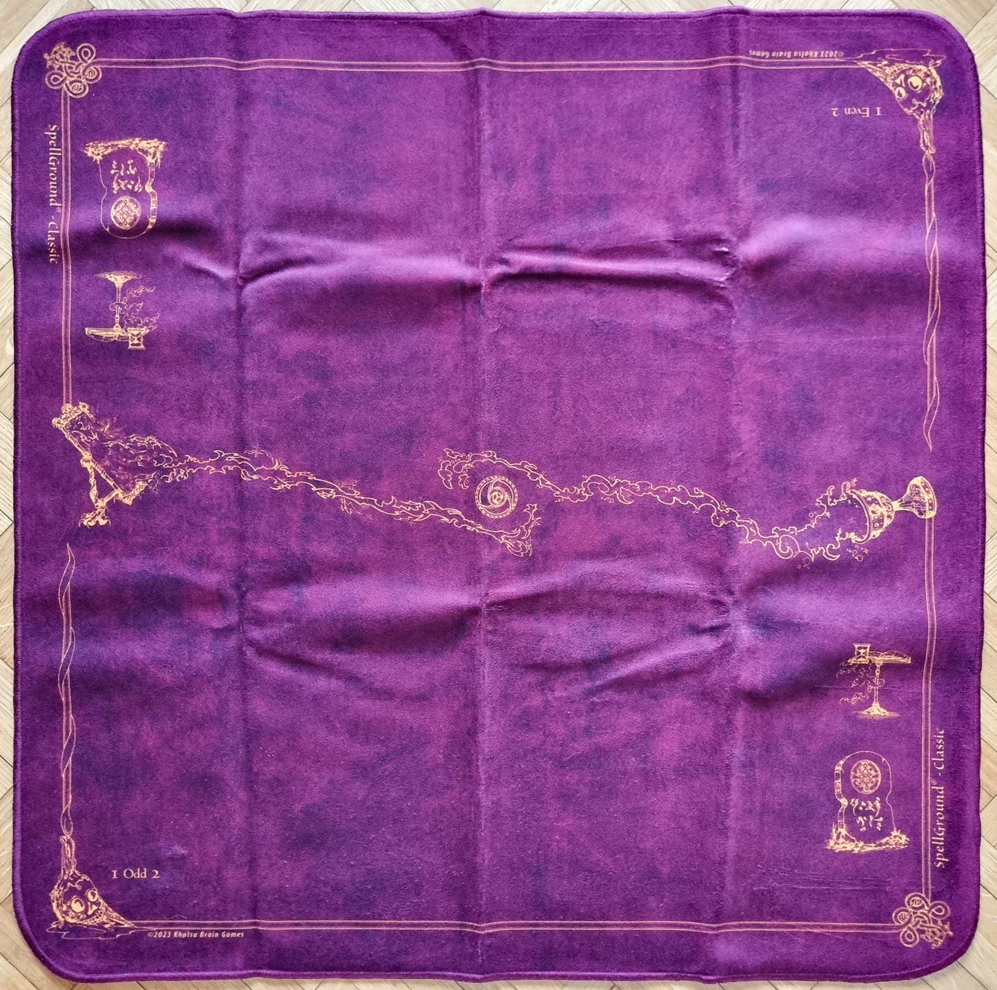 SpellGround V8 Classic Merlot 2-player playmat by Khalsa Brain Games, with wine-purple fabric, golden Classic line art, fantasy icons, and stitched edges.