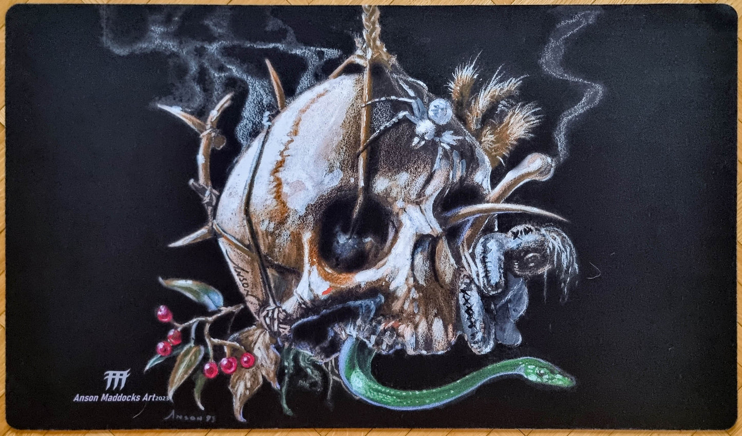 Signed Black Mana Battery playmat by Anson Maddocks featuring a spiked skull, green serpent, spider, bones, feathers, and berries against a black background.