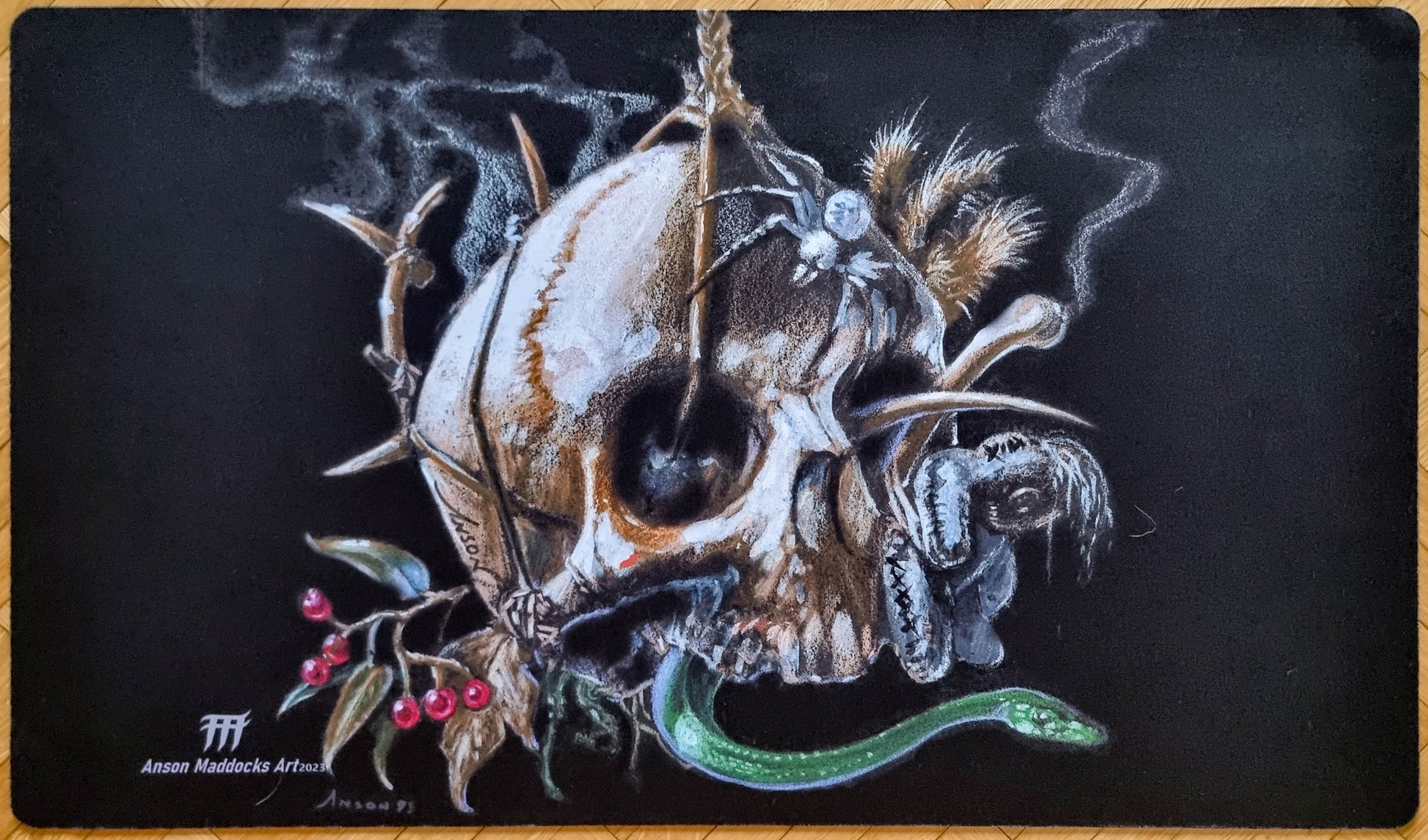 Signed Black Mana Battery playmat by Anson Maddocks featuring a spiked skull, green serpent, spider, bones, feathers, and berries against a black background.