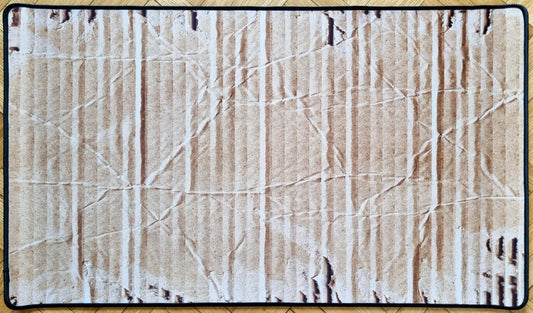 Stitched cardboard texture TCG playmat showing a realistic worn corrugated box surface with creases, vertical ribs, scuffs, and a black border.