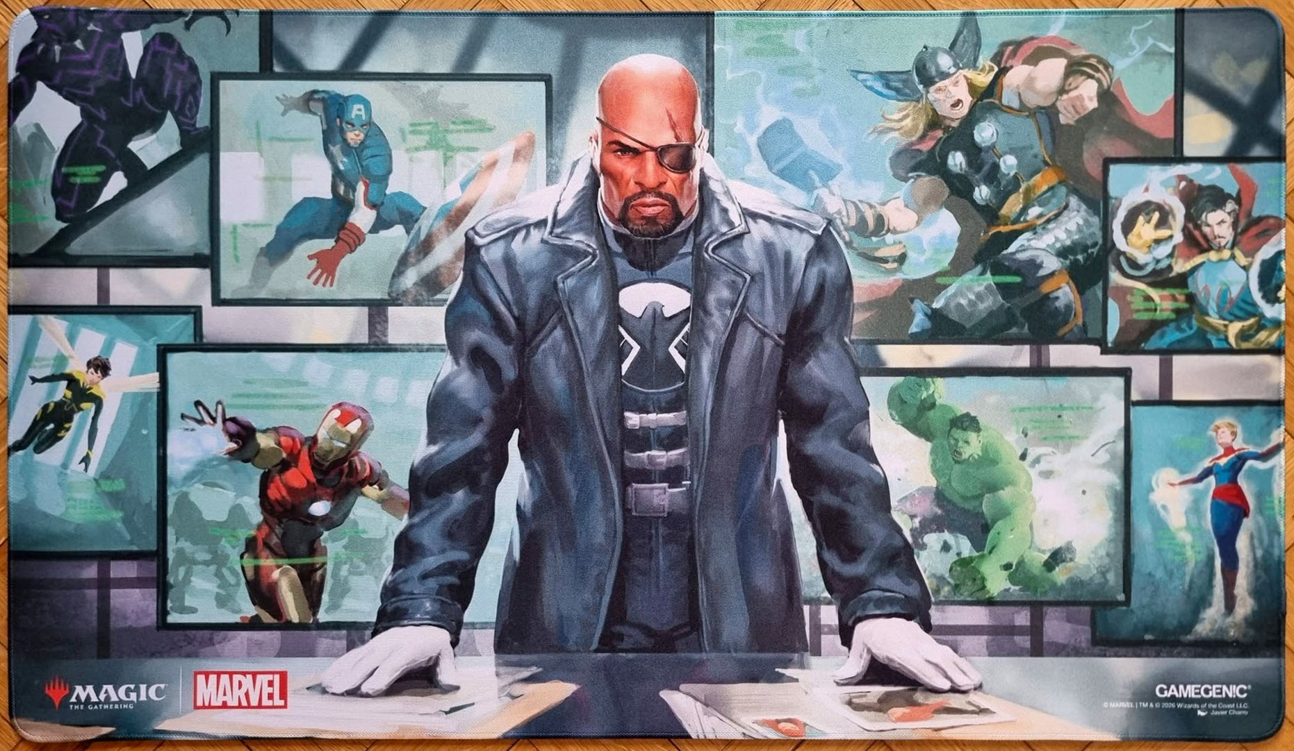 Magic: The Gathering x Marvel Director Nick Fury playmat featuring Javier Charro’s artwork, showing Nick Fury at a command desk surrounded by screens with Marvel heroes and stitched edges.