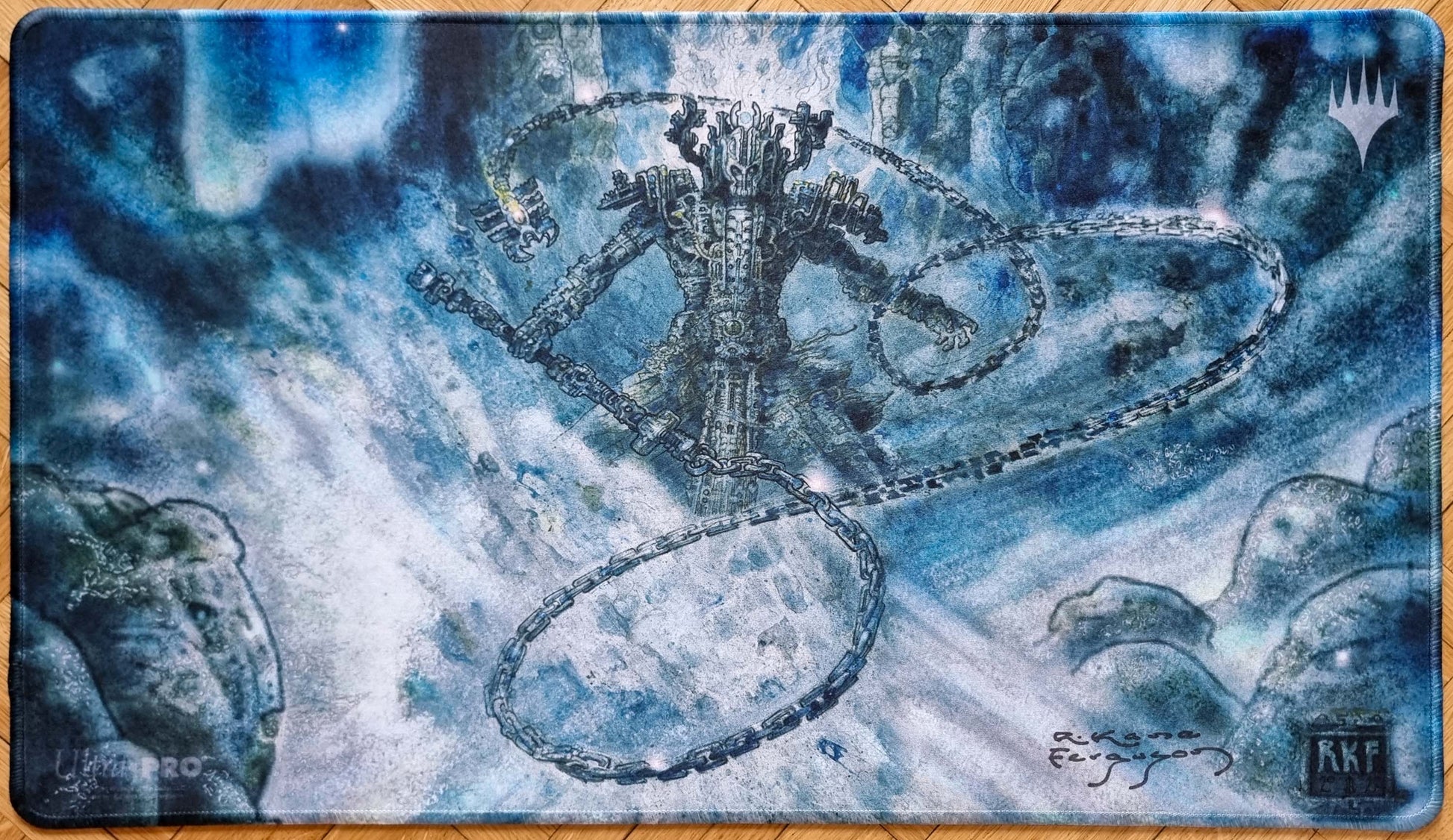 Signed stitched Grand Abolisher playmat by Richard Kane Ferguson featuring a blue-toned abstract figure surrounded by swirling chains from Commander Masters.