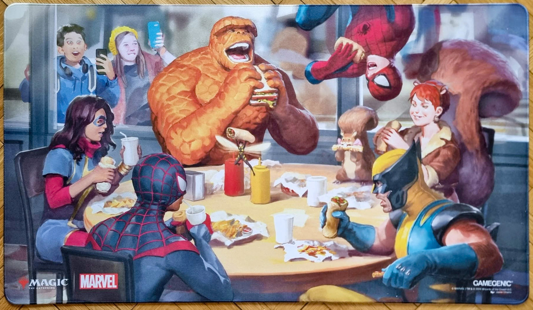 Magic: The Gathering x Marvel Heroic Feast playmat featuring Javier Charro’s artwork, showing Marvel heroes sharing a meal in a diner with stitched edges.