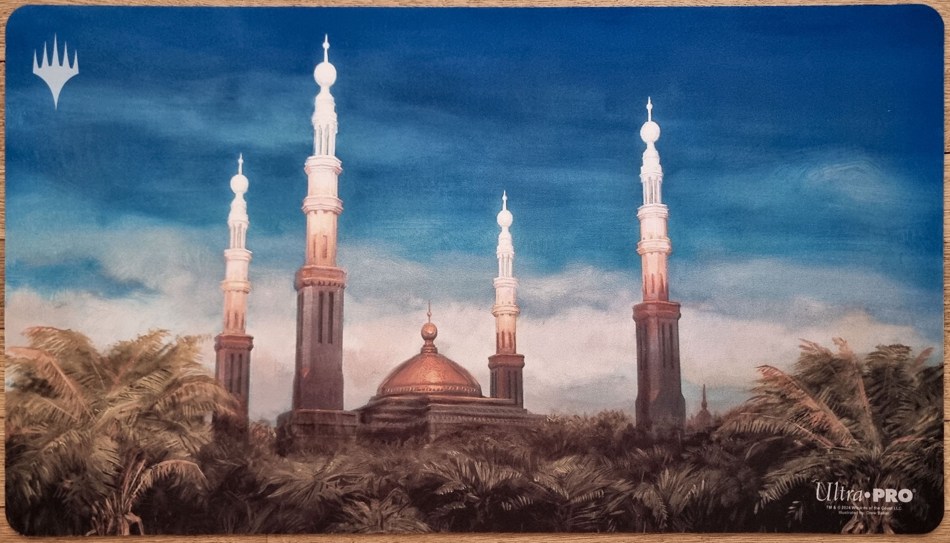 Karakas MTG playmat by Drew Baker showing a towered city with domes and palm trees under a calm blue sky.
