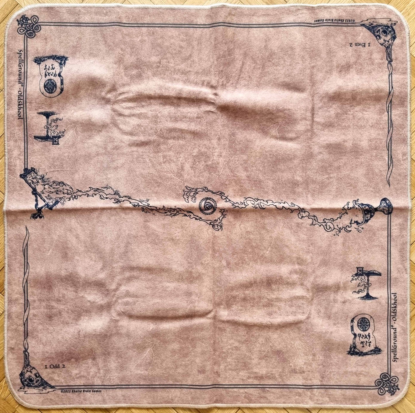 SpellGround V8 OldSkhool Tan 2-player playmat by Khalsa Brain Games, with mottled tan fabric, dark classic line art, fantasy icons, and stitched edges.