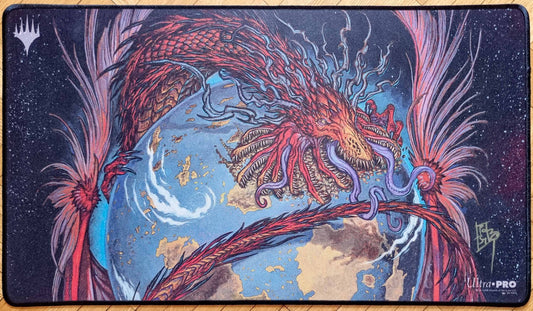 Signed Worldgorger Dragon MTG playmat featuring rk post’s Dominaria Remastered artwork, showing a red dragon coiled around a blue world with stitched black edges.